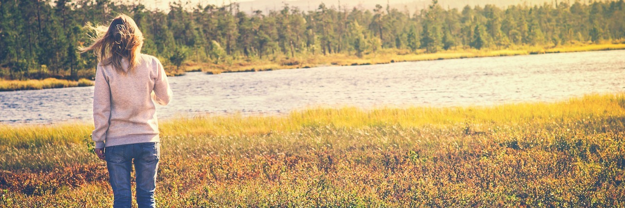 What Isolation Feels Like With Borderline Personality Disorder a woman standing in grass looking at a river