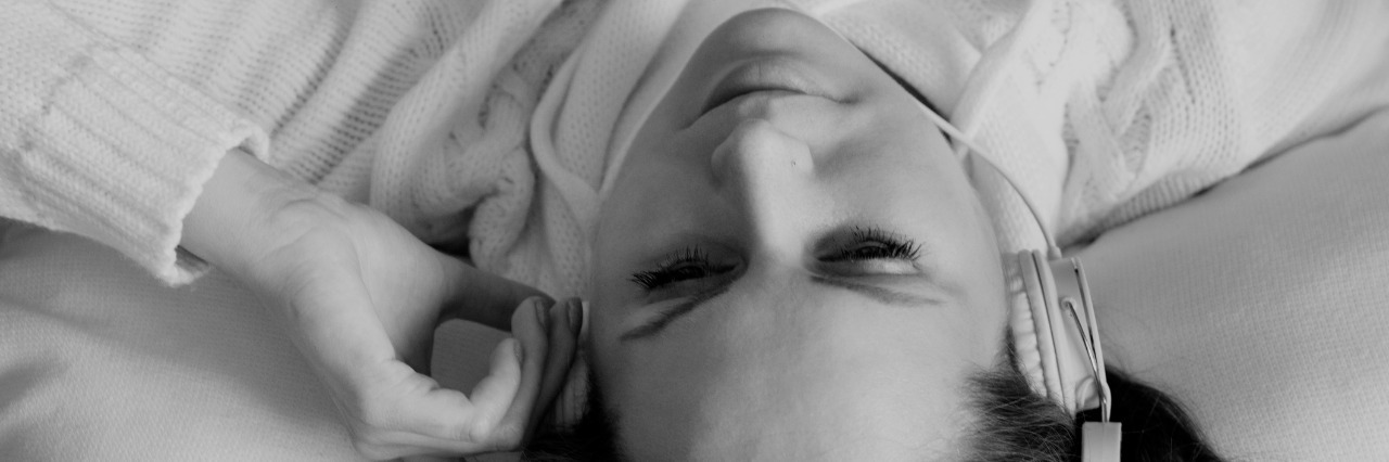 Young adult woman listening music with headphones in bed.