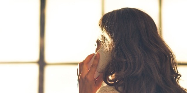 Woman talking on cell phone in front of window