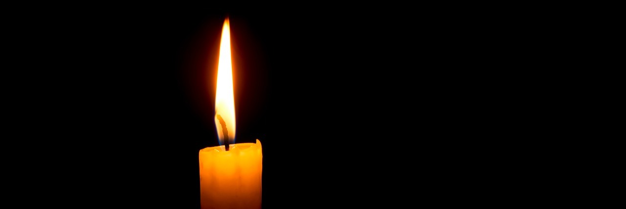 Grieving After a Miscarriage yellow single candle on a dark black background