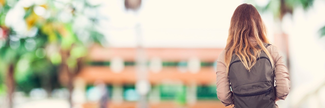 a girl with a backpack walking towards a school building