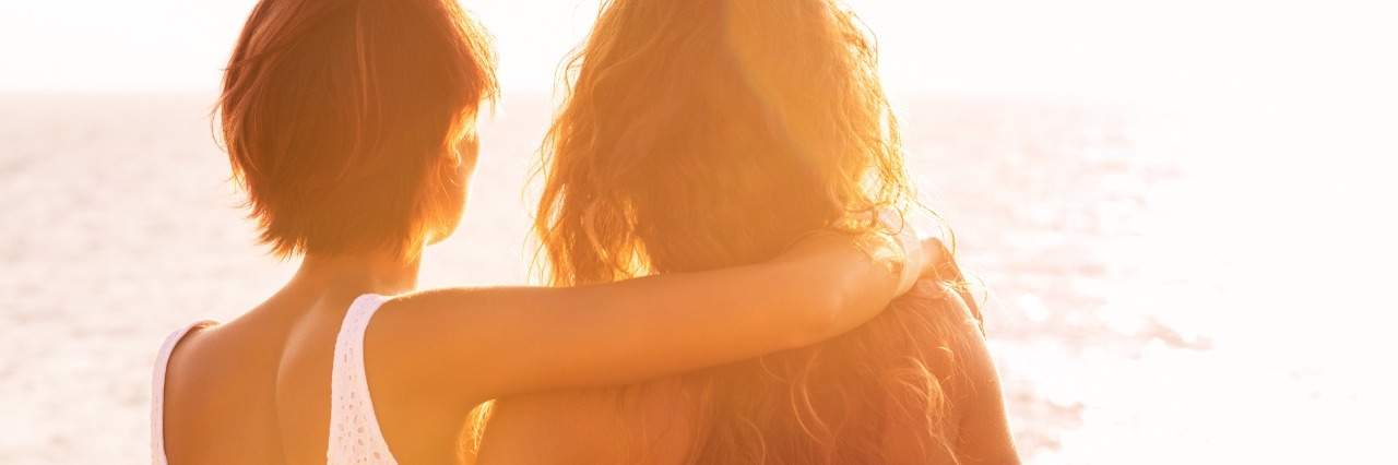 How to Support a Friend With Chronic Illness back view of two female friends hugging and looking out at the sea