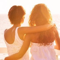 back view of two female friends hugging and looking out at the sea