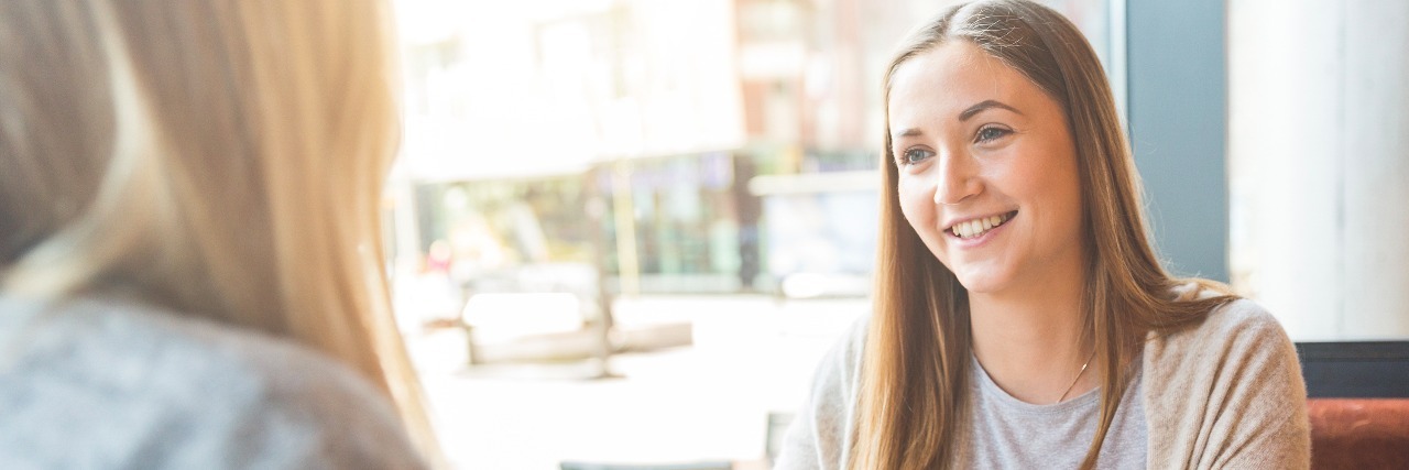 Why It's Difficult to Introduce Your Illness to Others Two beautiful young women in a cafe, drinking coffee and latte macchiato and talking. They are sitting in front of each other, and they are having fun together. Friendship and lifestyle concepts.