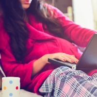 woman laying in bed with her PJs on watching a show on her laptop