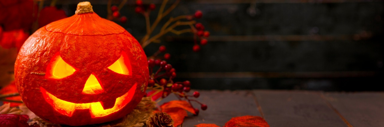 Burning Jack O'Lantern on a rustic table with autumn decorations, darkly lit.