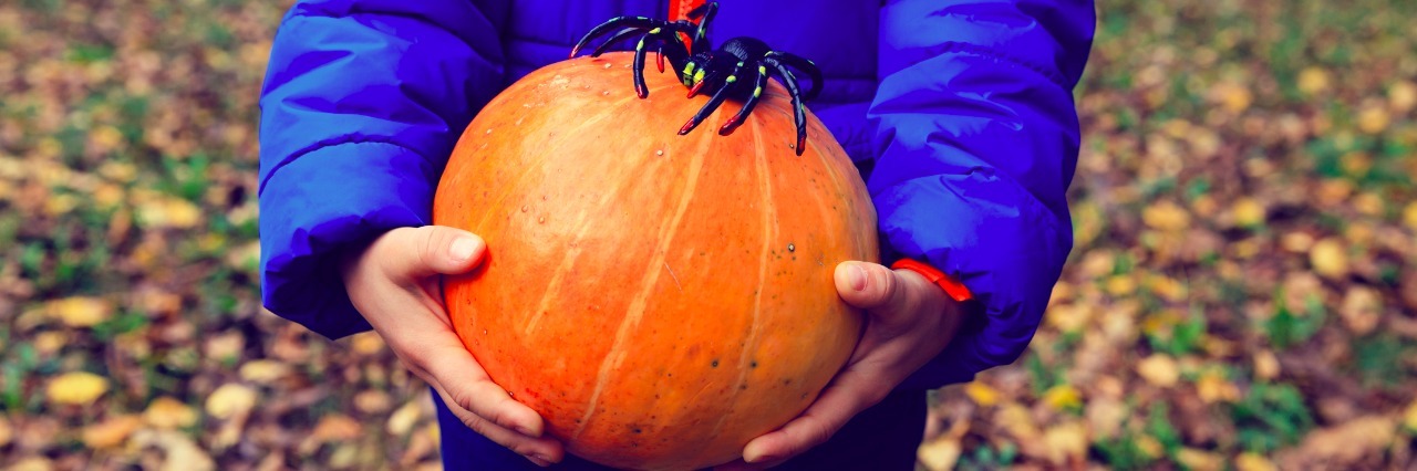 Autism and Halloween: Accepting That My Son Won't Wear a Costume child holding pumpkin with spider on fall leaves, halloween