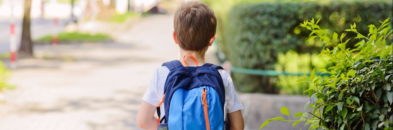 Little 7 years schoolboy going to school. Dressed in white t shirt and shorts. Blue backpack