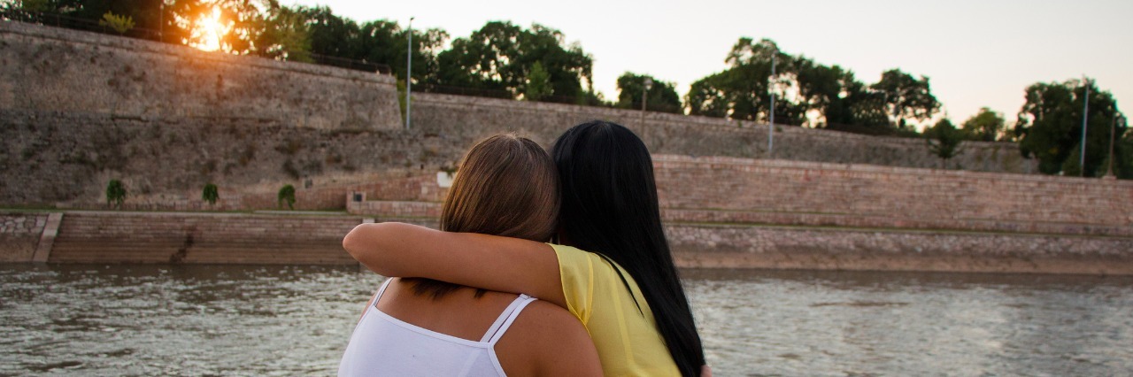 5 Ways to Help Someone in a Depressive Episode girls hugging each other overlooking a river at sunset