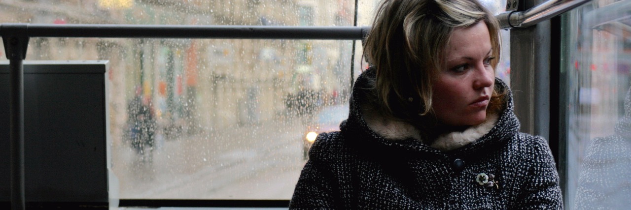 woman sitting alone on a bus and looking out the window on a rainy day