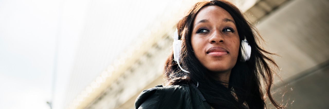 Songs Describing Menstrual Cycle of Woman With Endometriosis woman standing outside in sunlight with headphones on listening to music