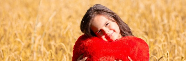 Little girl with heart shaped pillow in the wheat field. Girl cuddling with heart