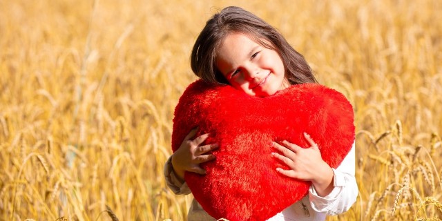 Little girl with heart shaped pillow in the wheat field. Girl cuddling with heart