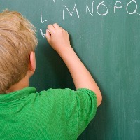 a young boy writing out the alphabet on a chalkboard