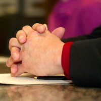 Close-up of folded hands on a table at a meeting