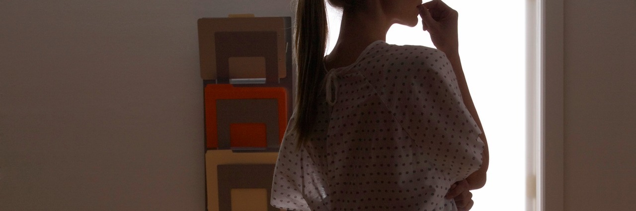 5150: My Experience Being Hospitalized After a Suicide Attempt a woman wearing a hospital gown standing in shadows