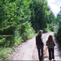 Mother and daughter walking dog on road through forest