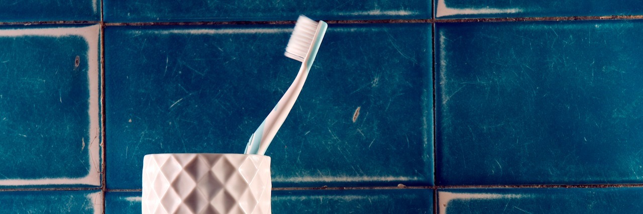 A tooth brush in container on a shelf of a bathroom