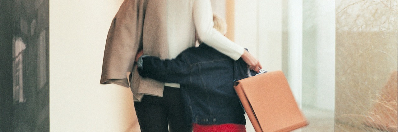 Woman holding briefcase, walking down a hallway with her arm around her son
