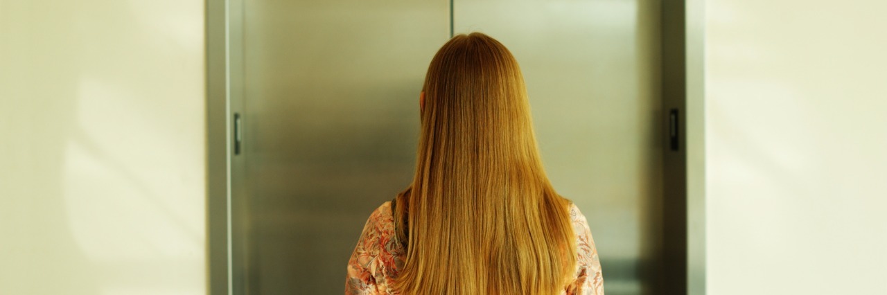 How Others Treat You When You Have an Invisible Illness back of a blonde woman waiting for the elevator