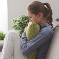 Lonely depressed woman at home, she is sitting on the sofa and hugging a pillow