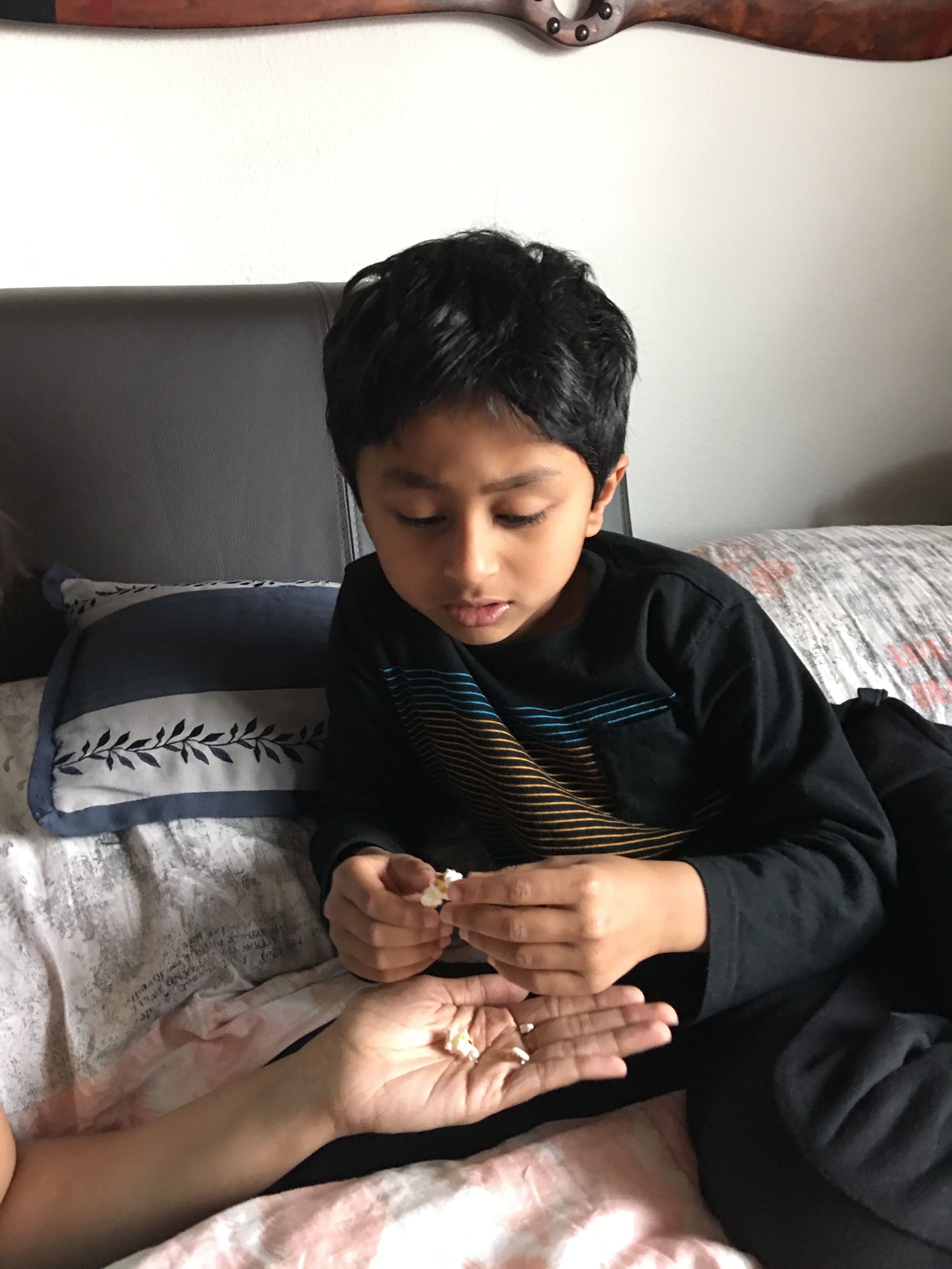 Boy on bed, taking popcorn from someone's hand