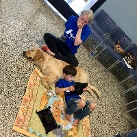 Mother crying and holding a hand to her mouth as her son lies against his new service dog