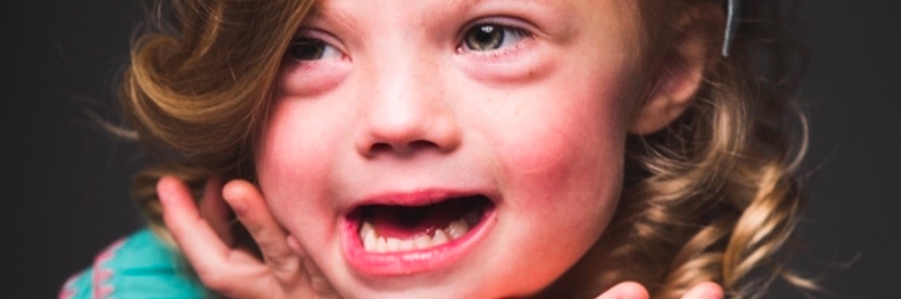 Down Syndrome Awareness Month: Sharing My Baby's Diagnosis Story Girl smiling for photo with palms under her chin