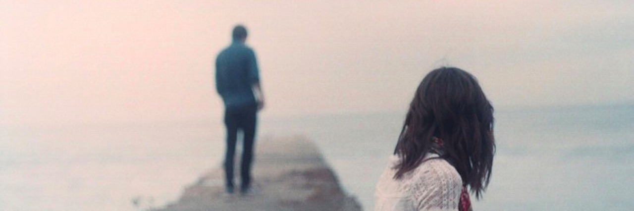 What My Marriage Looks Like After My Husband's PTSD Diagnosis a woman looks at a man standing away from her on a lonely path