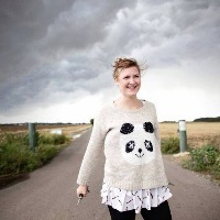 woman wearing a panda sweater walks down a road with dark storm clouds behind her