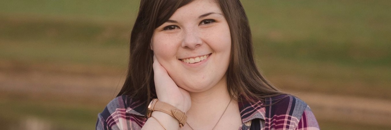 Positive Body Image as Woman With Crohn's Disease and Ostomy Scars young woman standing in front of a lake and wearing an open flannel jacket with visible scars on her stomach