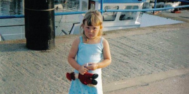 young girl holding toy standing on dock