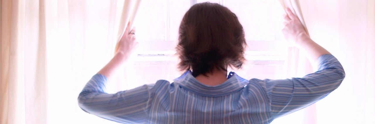 Don’t Say ‘At Least It’s Not…’ When Talking About Someone’s Health woman opens curtains as she looks out a window