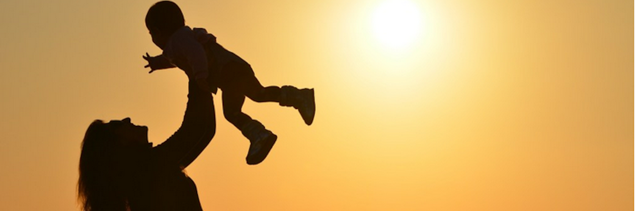 Woman standing on beach at sunrise holding her baby over her head