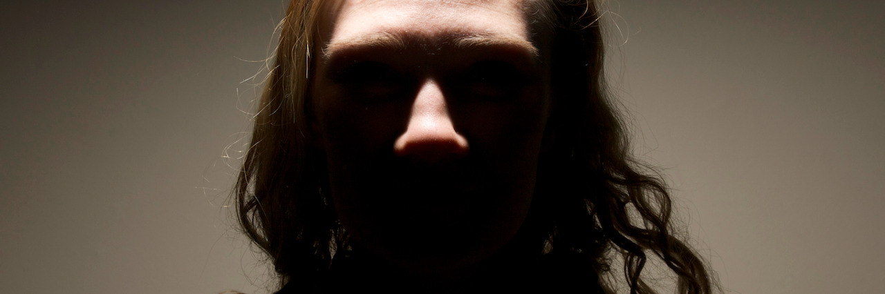 When Depression Comes Back Again A sinister looking girl, with king-pin villain lighting. Eyes not visible, silhouette of her shape with muted colours and plain background.