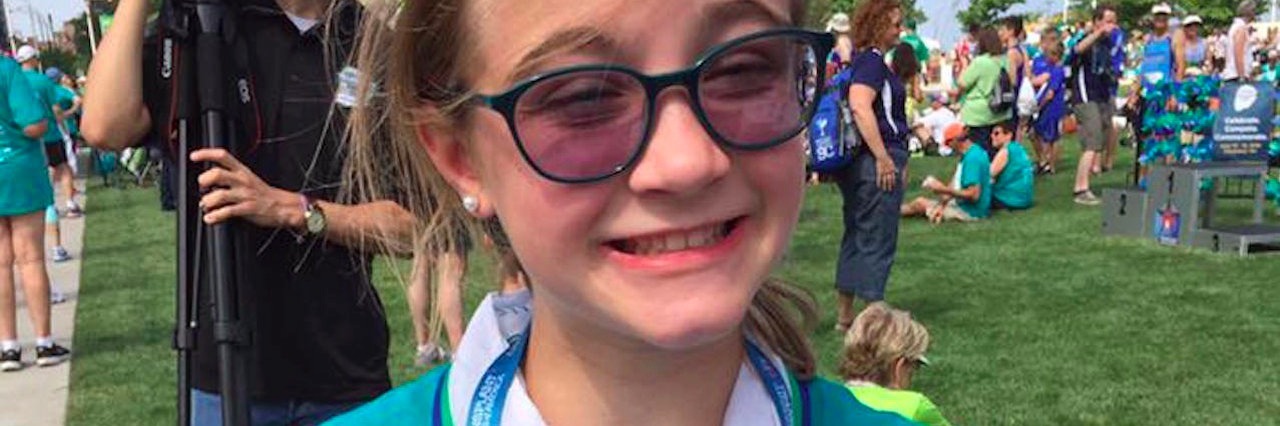 Letter to Trump, From the Mother of a Chronically Ill Daughter girl wearing a medal and giving a thumbs up