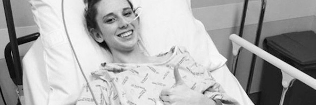 young woman give a thumb’s up while lying in a hospital bed