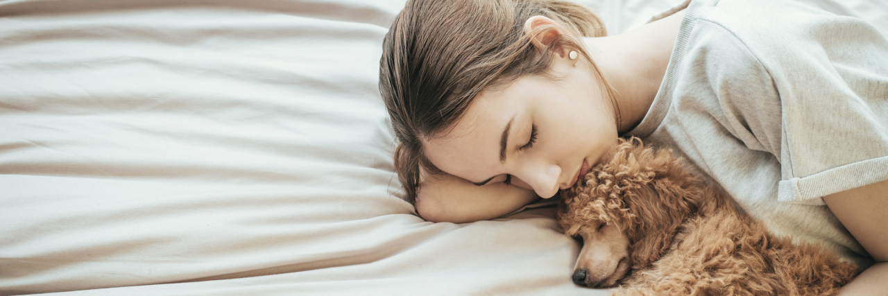 Having to Take Naps With Crohn's Disease Young woman is lying and sleeping with poodle dog in bed.