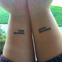 A womans shows her tattoos on both her wrists that say, "Just breathe," and "Move forward."