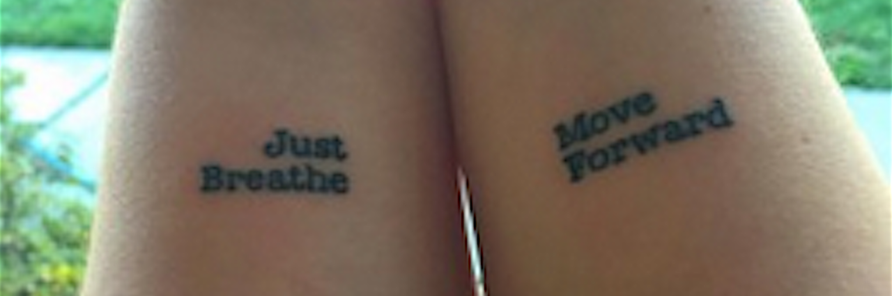 A woman's forearms with two tattoos along her wrists that say, "Just breathe," and "Move forward."