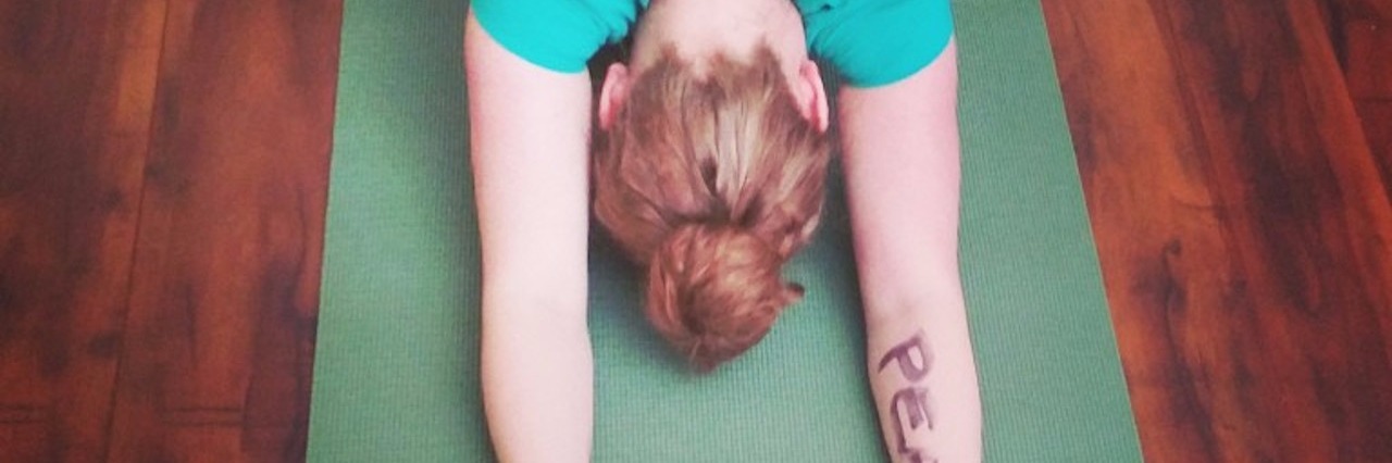woman in blue shirt doing yoga pose with 'peace' written on her arm