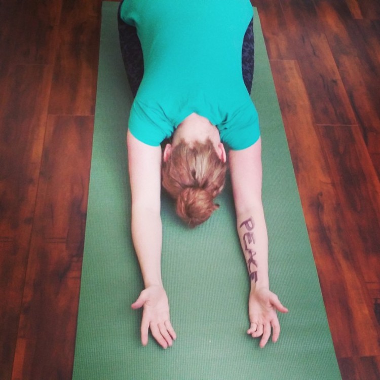 woman in blue shirt doing yoga pose with 'peace' written on her arm