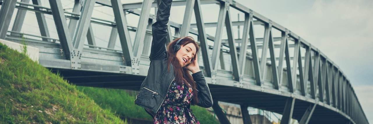 woman wearing headphones dancing near a bridge