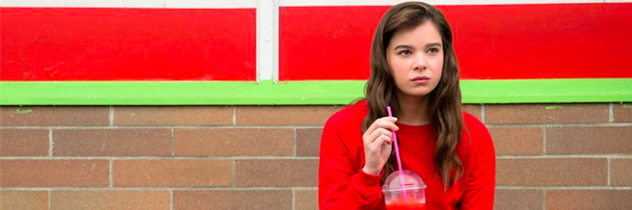 A young girl sitting on the edge of a sidewalk sipping a slurpee