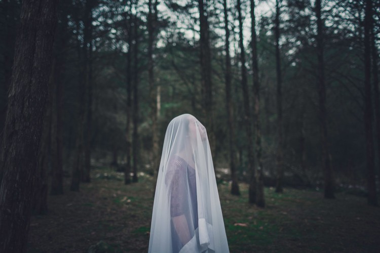 woman standing in forest with sheer white sheet over her head and face