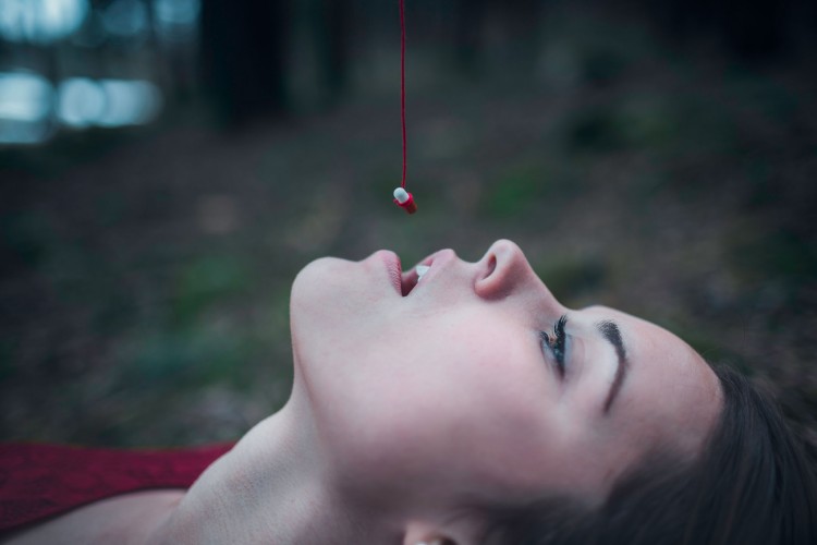 girl laying back with pill attached to string held over her mouth
