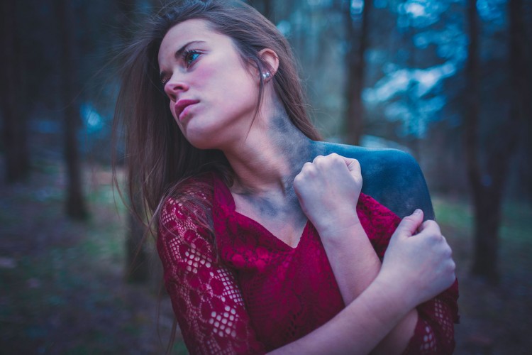 woman wearing red dress covered in black ash on one shoulder and side of neck