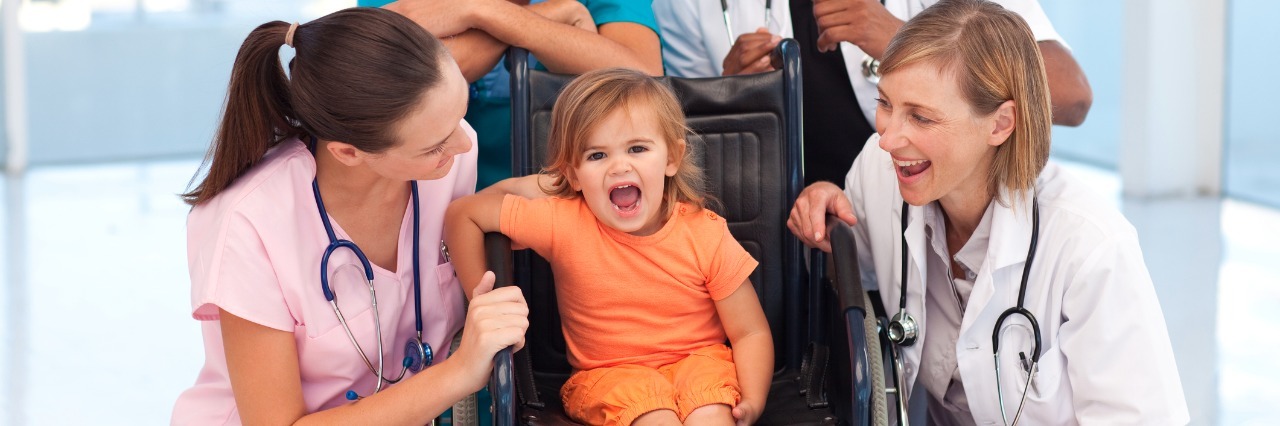 Group of doctors playing with a baby in a wheelchair