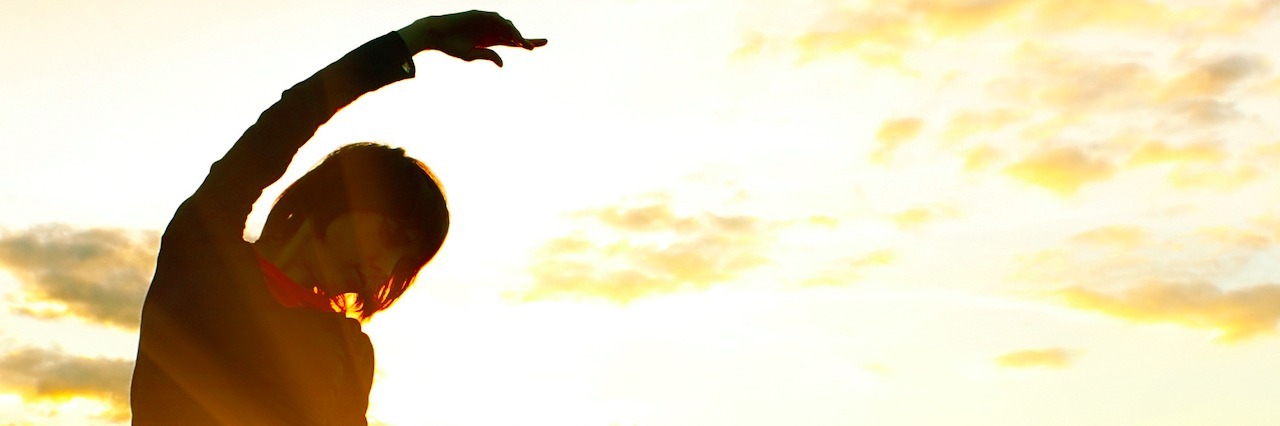 How to Take Care of Yourself When You Live With a Mental Illness A woman standing in a field of flowers at sunset