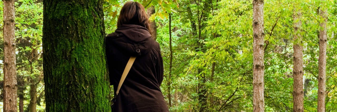 Why It's Difficult for Me to Describe My Anxiety to Others Woman wearing long coat, leaning against tree in park